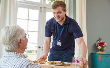 Carer bringing a tray of food to a customer